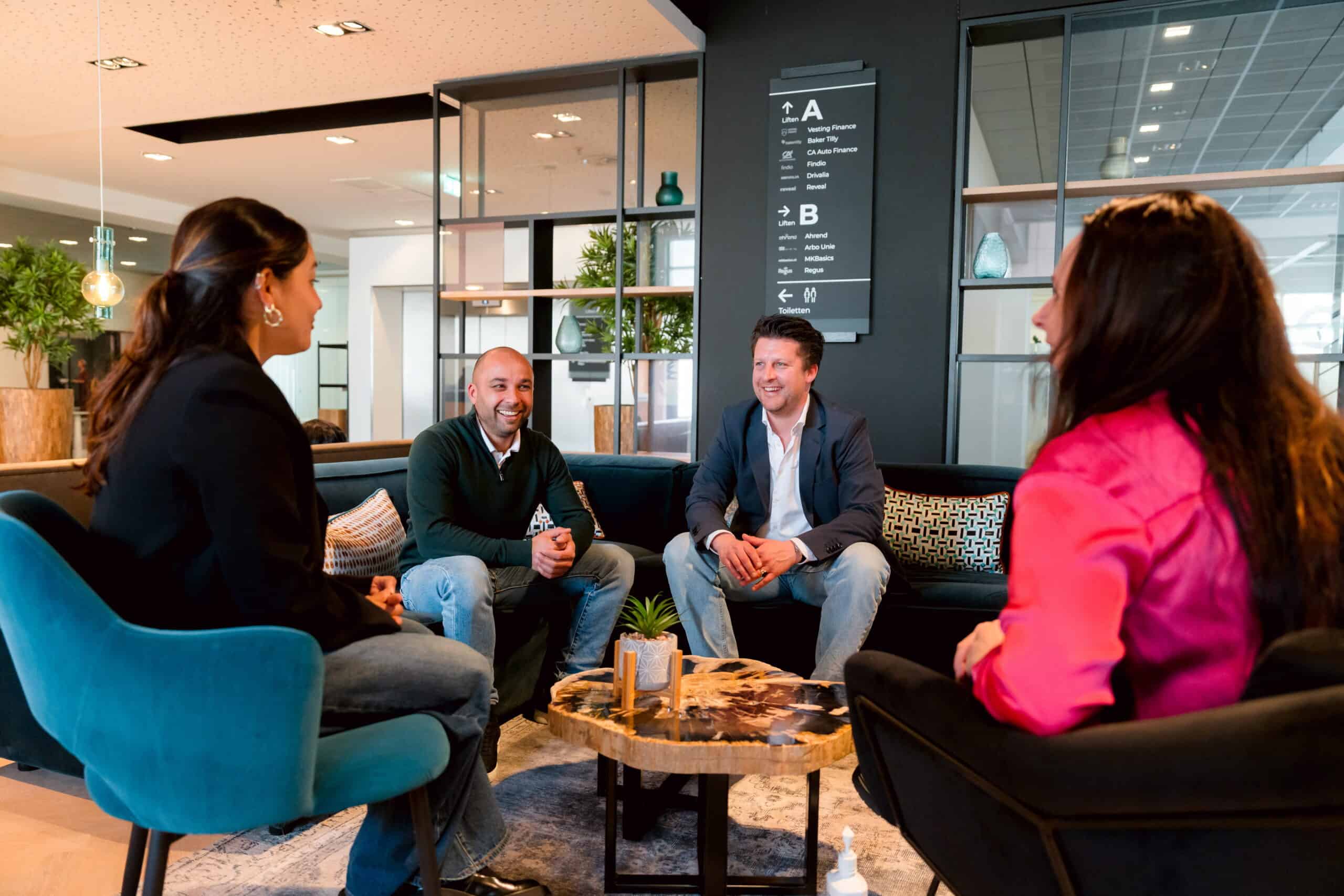 Vier mensen in gesprek rond een salontafel in een kantoorlounge