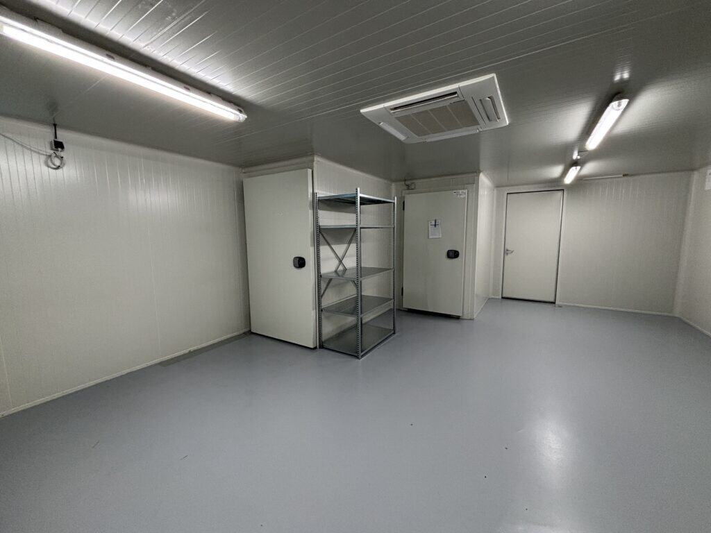 Lege opslagruimte met witte wandpanelen, koelceldeuren en een metalen stellingkast